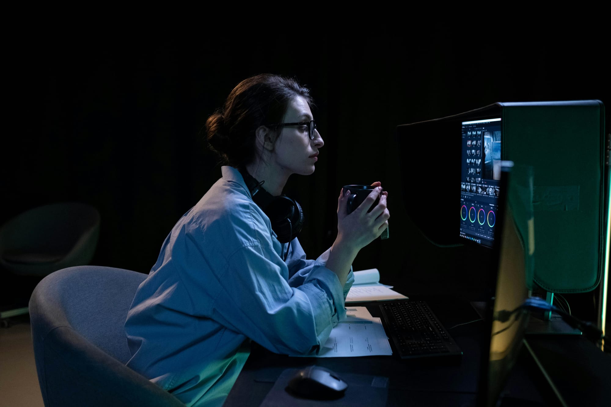 Woman sitting in dark room hoding coffee mug and looking at computer screens